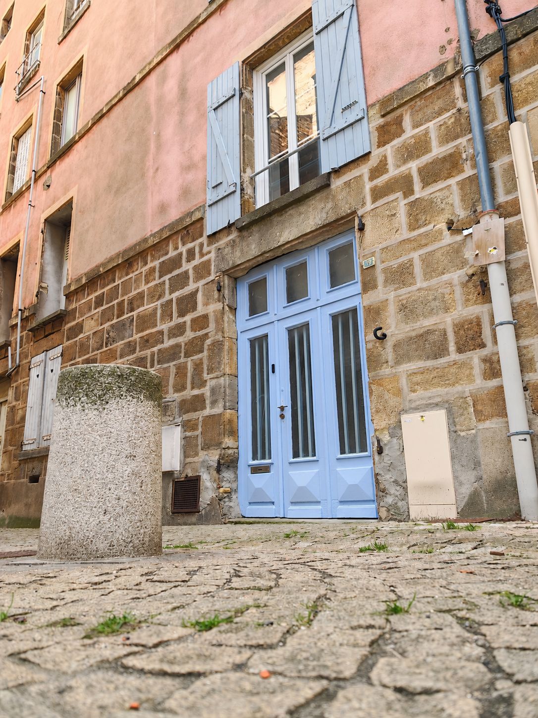 A stone building with a blue door and shutters, a stone pillar, and a metal utility box.