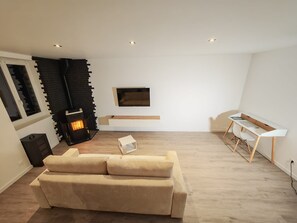Ein modernes Wohnzimmer mit einer Couch, einem Kamin, einem an der Wand befestigten Fernseher und einem Schreibtisch.