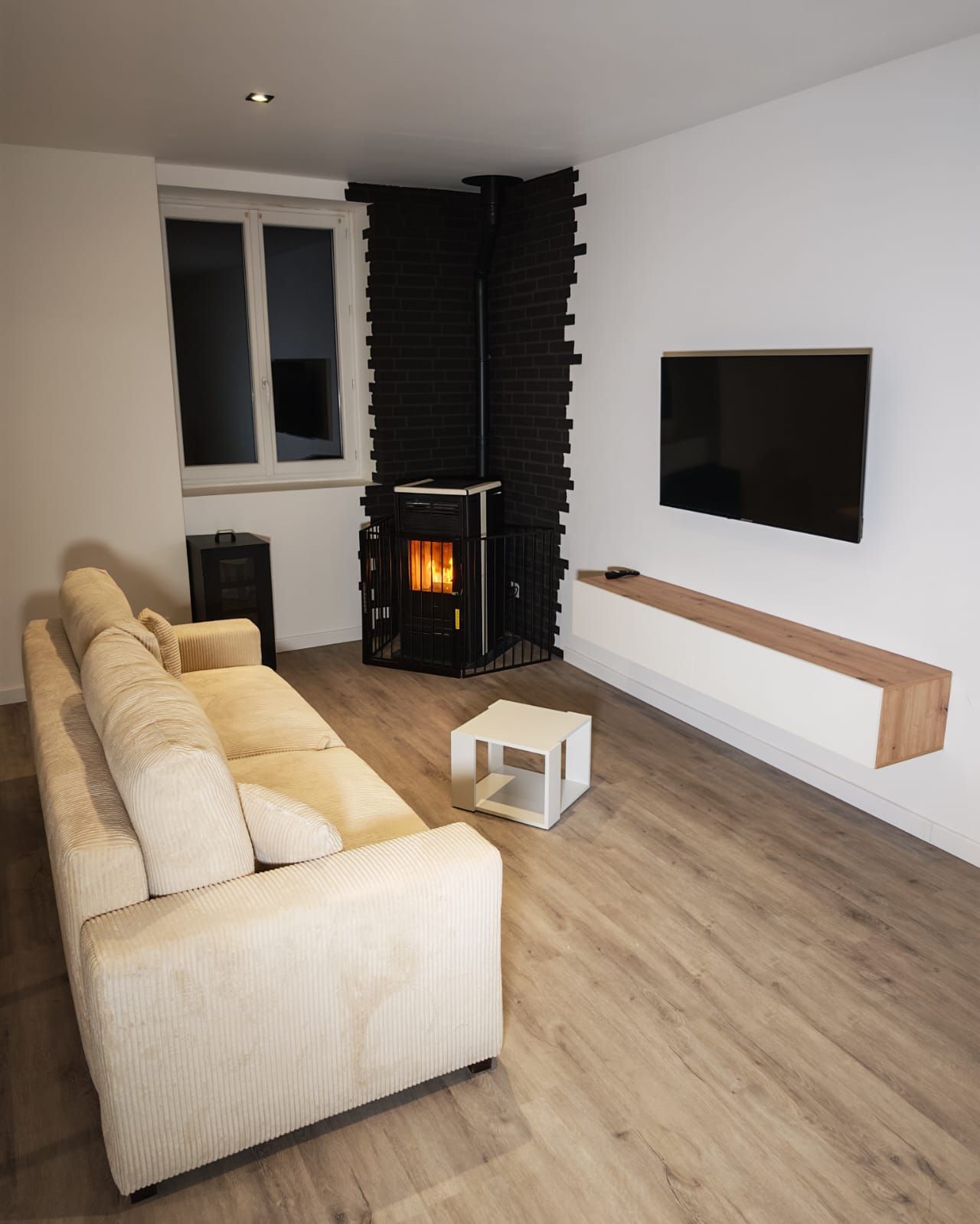 Una sala de estar moderna con un sofá seccional, una chimenea negra, un televisor montado en la pared y un estante de madera.