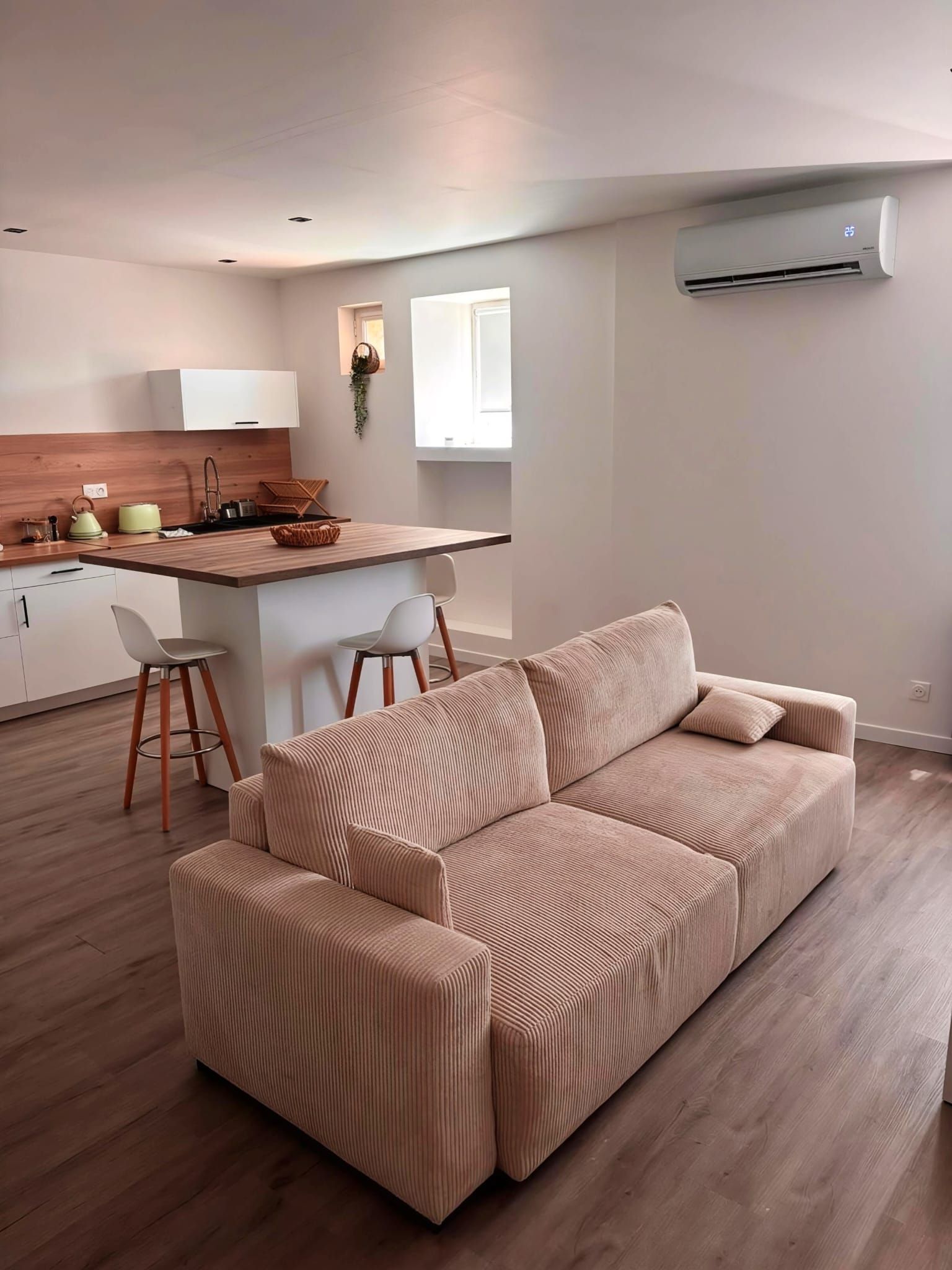 Un salon moderne avec un canapé, un coin cuisine doté d’un plan de travail en bois et une fenêtre.
