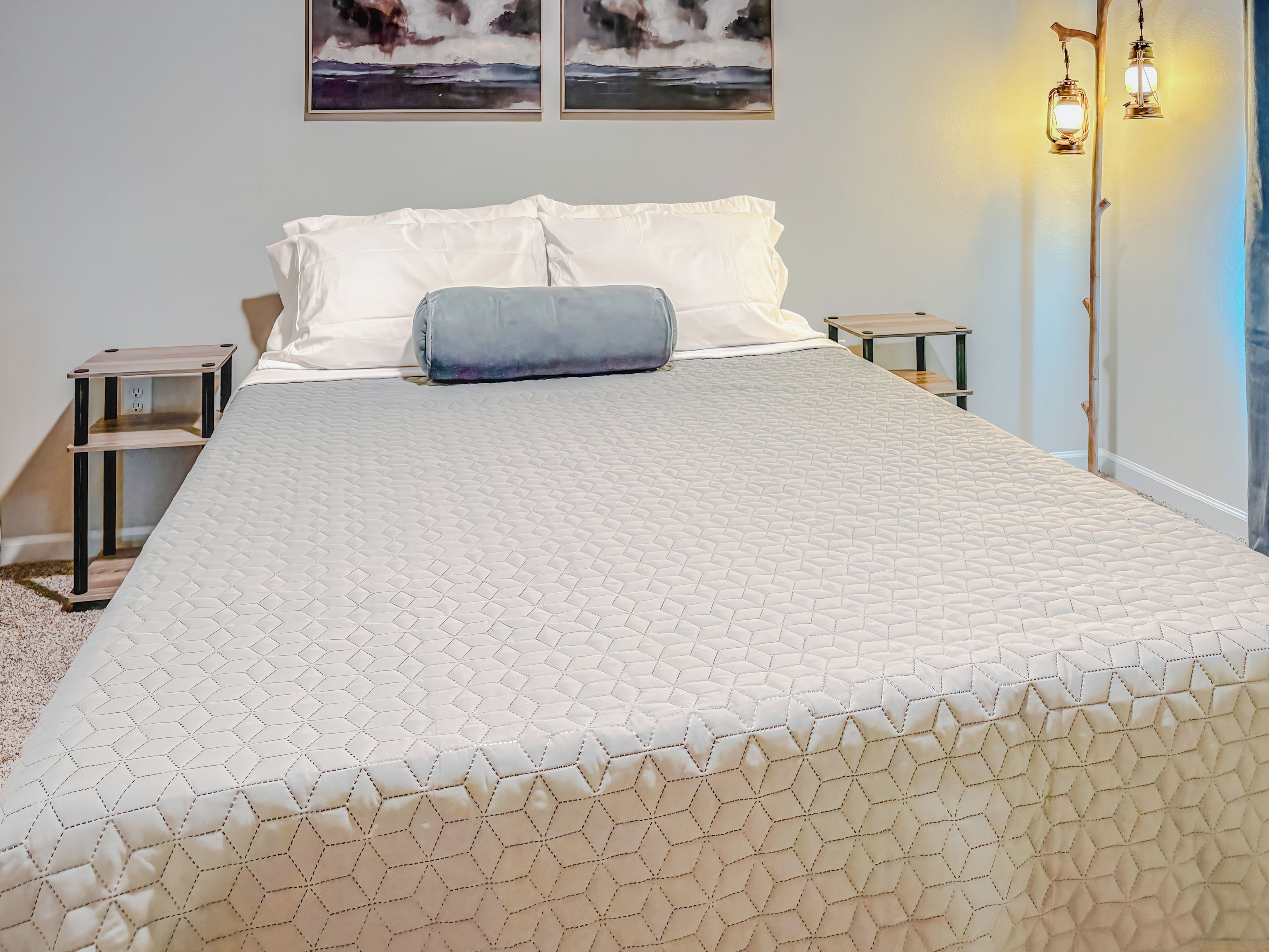 A neatly made bed with a quilted headboard, two bedside tables, and wall-mounted lamps.