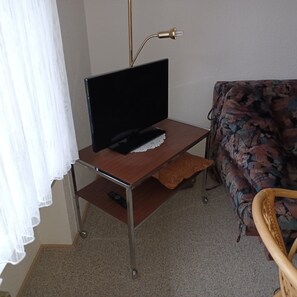 A room with a television on a wooden stand, a remote control on the stand, a floral sofa, and a curtain partially drawn. - Apartment '2' with Shared Terrace, Shared Garden and Wi-Fi (Goslar)