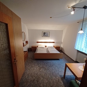 Een slaapkamer met een bed, nachtkastjes, een houten kledingkast, een lijst met een afbeelding aan de muur en een raam met gordijnen.
