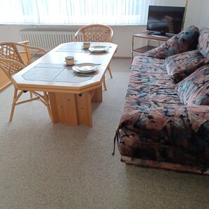 Ein Wohnzimmer mit einem Holzesstisch, Stühlen, einer Couch und einem Fernseher.