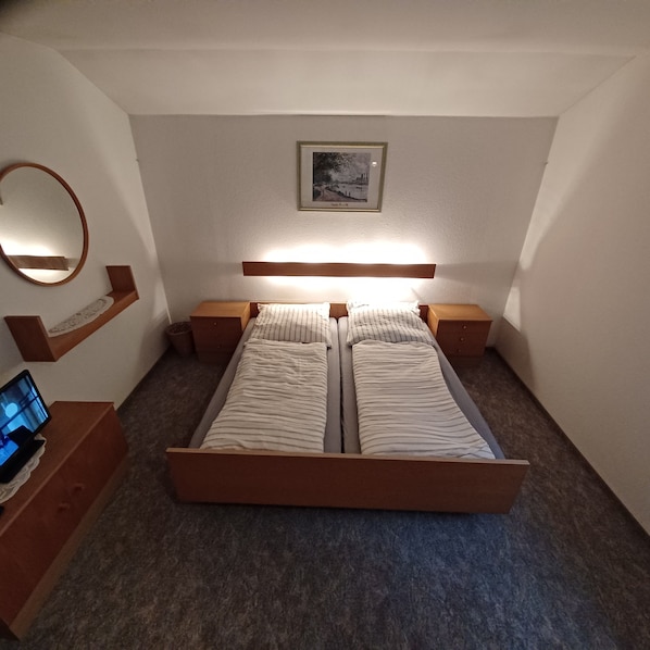 Une chambre à coucher avec un lit en bois, des tables de chevet, une commode, un miroir fixé au mur et un tableau encadré.
