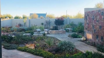 Un patio al aire libre con piso de baldosas, rodeado de plantas y un muro de ladrillo.
