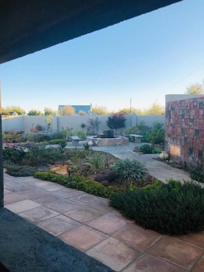 Un espace extérieur aménagé en terrasse, doté d’un sol carrelé, entouré de différentes plantes et bordé d’un mur en briques.
