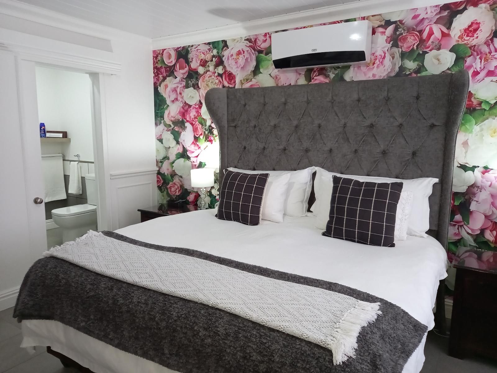 A bedroom with a large bed, a grey upholstered headboard, and a floral wallpaper.