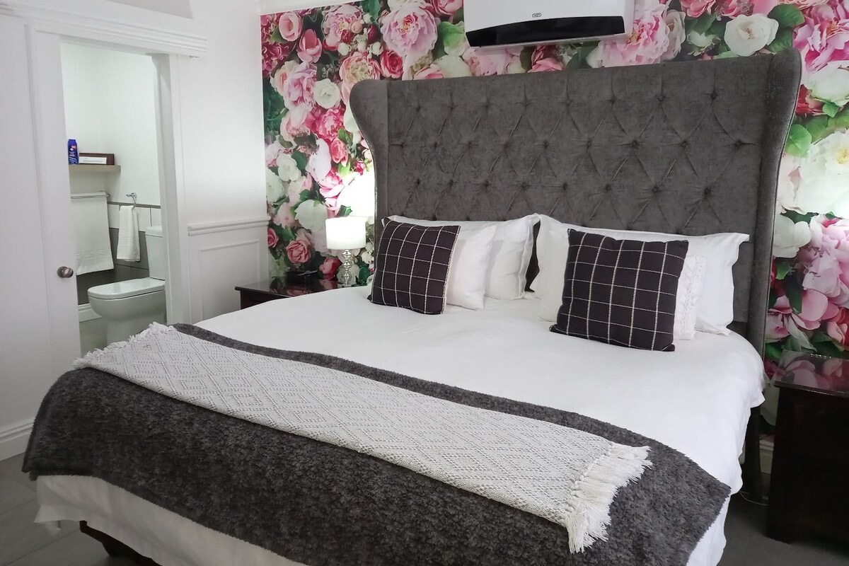 A bedroom with a large bed, a grey upholstered headboard, and a floral wallpaper.