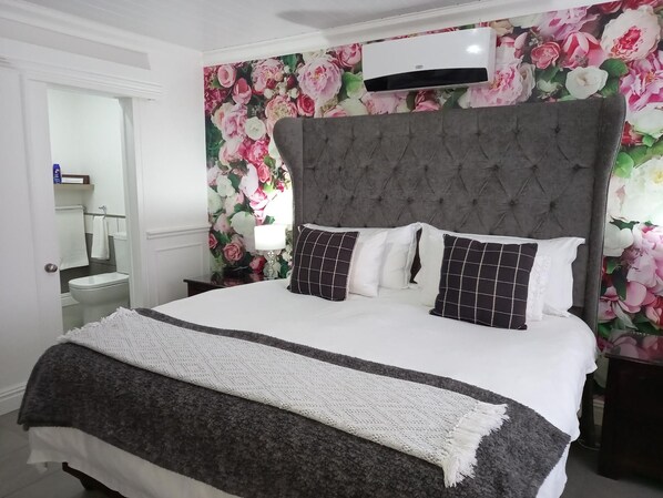 A bedroom with a large bed, a grey upholstered headboard, and a floral wallpaper.