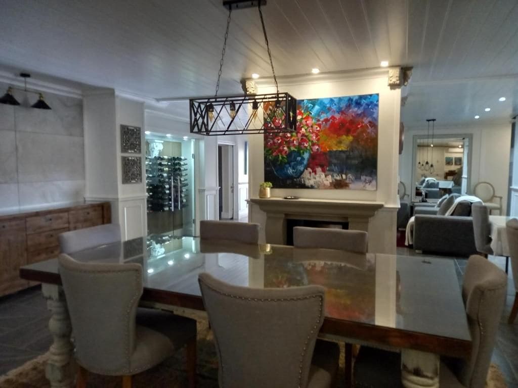 A dining area with a glass table and chairs, a fireplace, and a colorful painting on the wall.