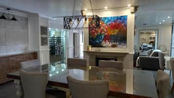 A dining area with a glass table and chairs, a fireplace, and a colorful painting on the wall.