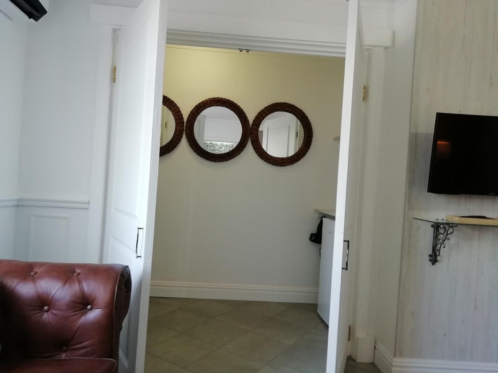 A hallway with a brown leather chair, a television mounted on the wall, and three circular mirrors.