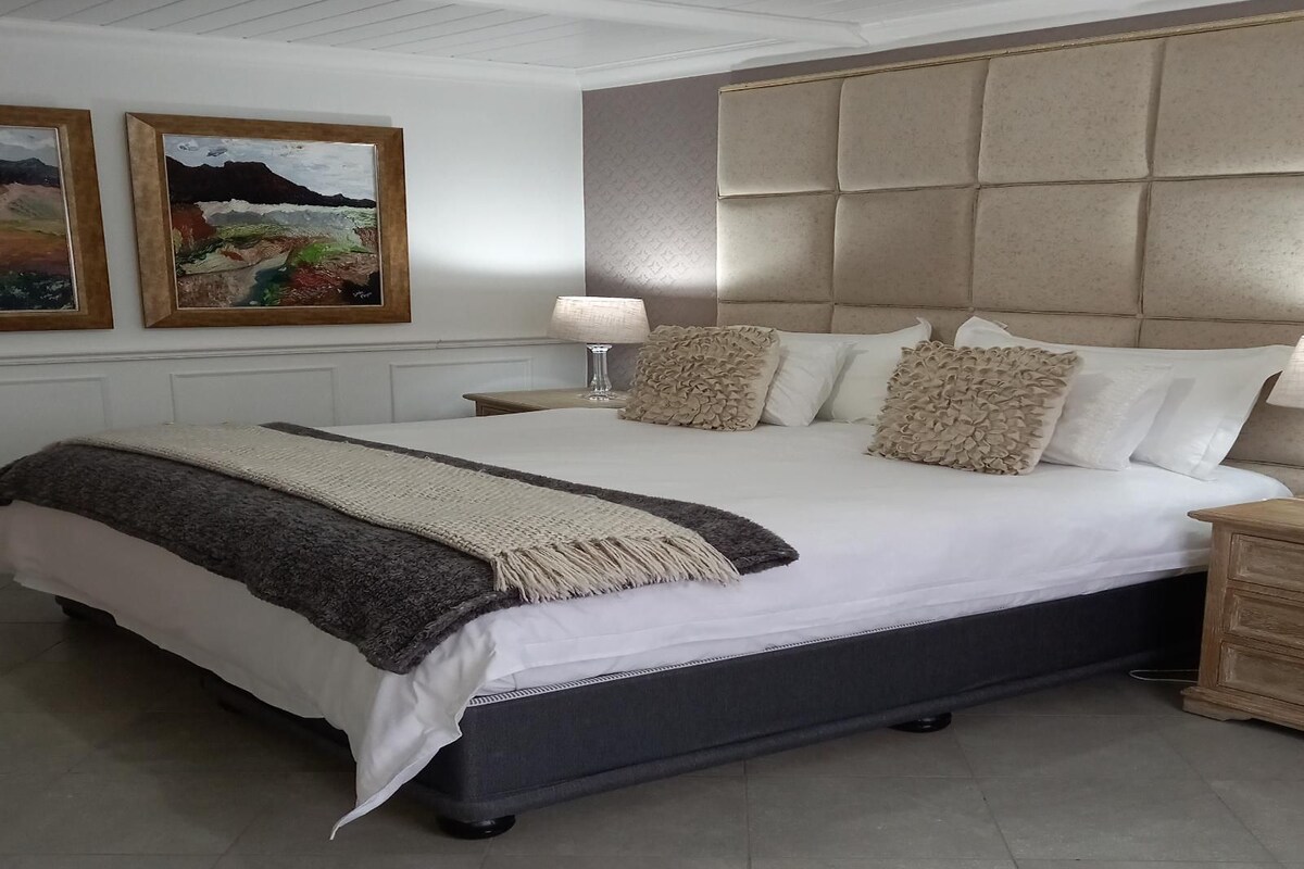 A bedroom with a large bed, a headboard, a bedside table with a lamp, and two framed pictures on the wall.