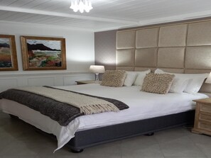 A bedroom with a large bed, a headboard, a bedside table with a lamp, and two framed pictures on the wall. - Linda se Dop (Nieuwoudtville)