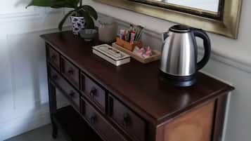 A wooden dresser with drawers, a potted plant, a coffee pot, and a mirror on the wall.