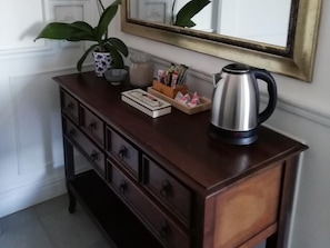 Une commode en bois avec des tiroirs, une plante en pot, une cafetière et un miroir accroché au mur.