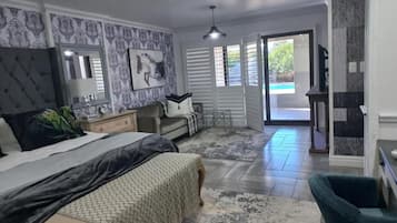 Un dormitorio amplio con una cama grande, una zona de estar con una silla, un tocador y vistas a una piscina a través de la puerta.