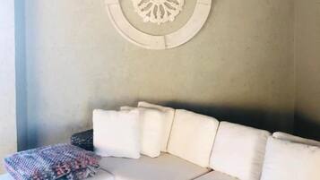 A corner of a room with a white sofa, a woven bench, and a decorative wall piece.