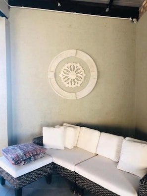 Un coin de pièce avec un canapé blanc, un banc en osier et un élément décoratif mural.
