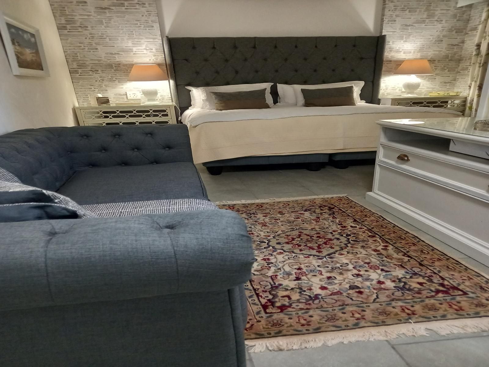 A bedroom with a bed, a grey sofa, a patterned rug, and a dresser.