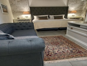 A bedroom with a bed, a grey sofa, a patterned rug, and a dresser.