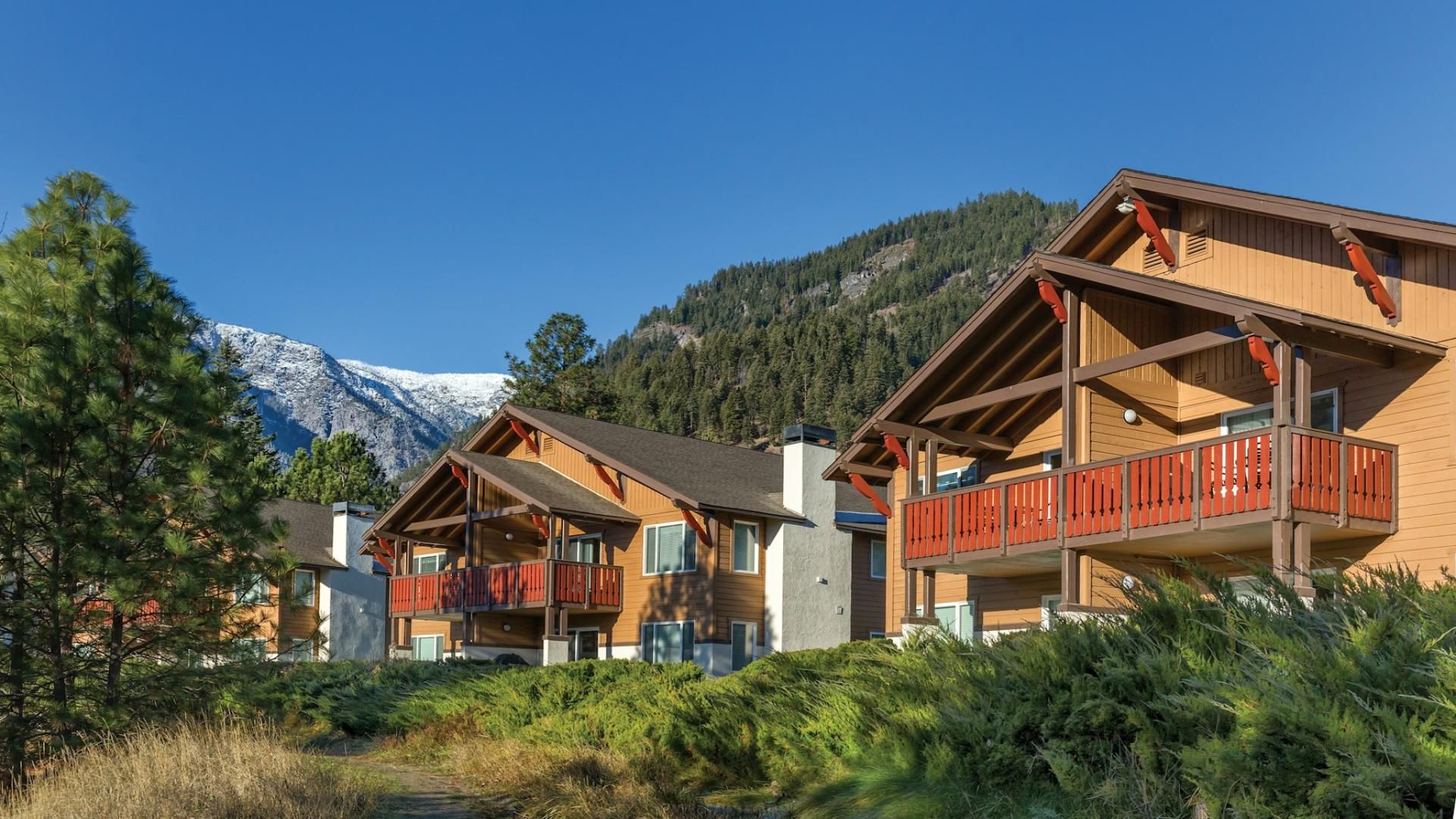 Eine Reihe von Blockhütten im Chalet-Stil mit Balkonen, vor einer Kulisse aus schneebedeckten Bergen und dichtem Wald.