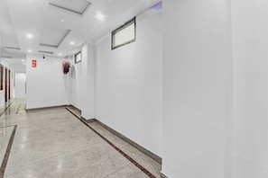 Um corredor com paredes brancas, chão ladrilhado e um hidrante fixado na parede.