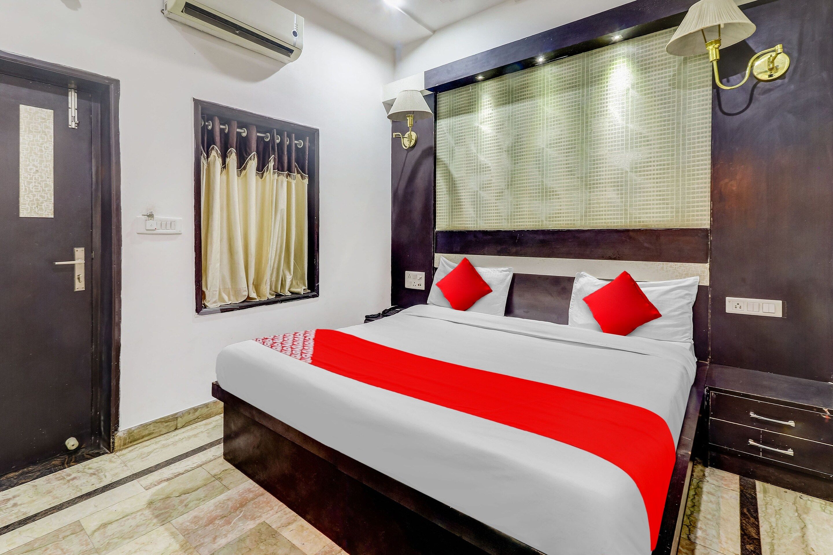 Una habitación de hotel con una cama, una ventana con cortinas, un equipo de aire acondicionado y una mesita de noche.