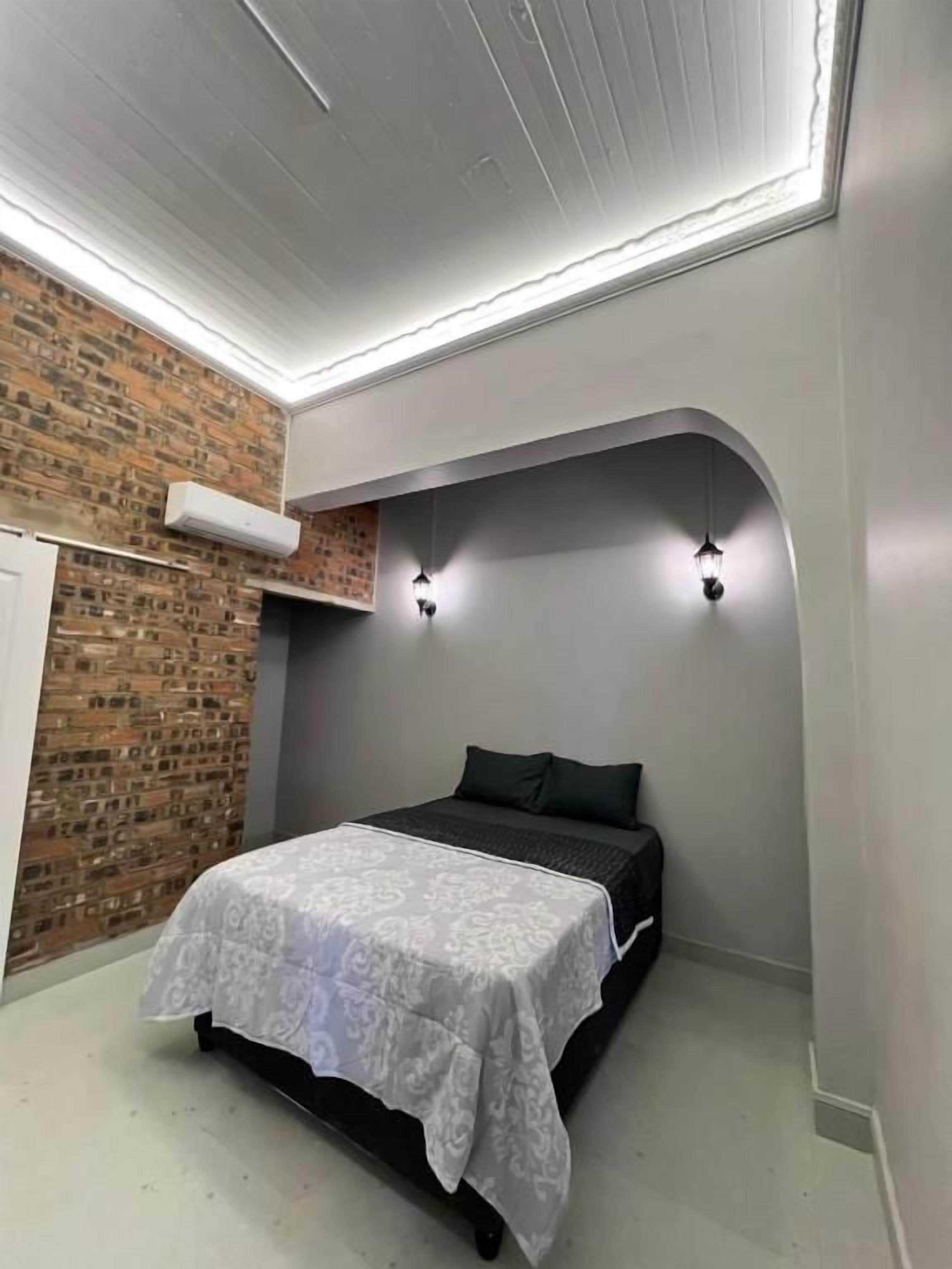 A bedroom with a bed, a brick wall, and a white ceiling.