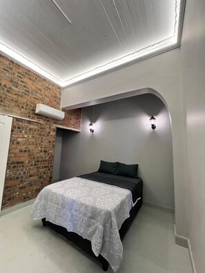 Un dormitorio con cama, pared de ladrillo y techo blanco.