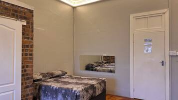 Un dormitorio con cama, espejo, puerta y pared de ladrillo.