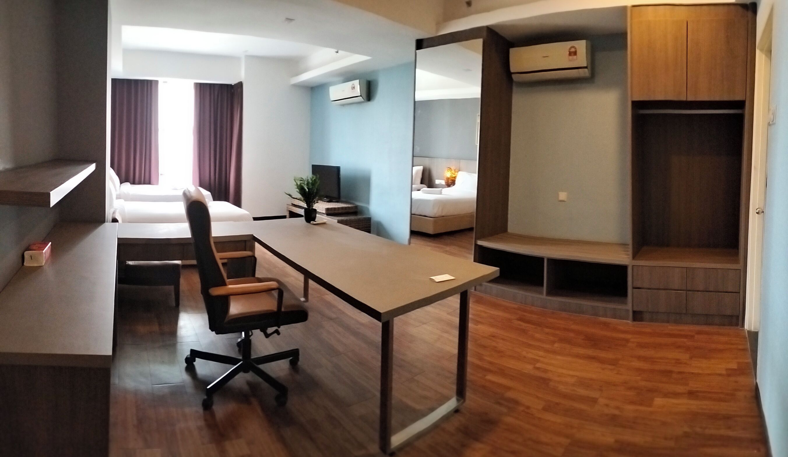 Ein Hotelzimmer mit Schreibtisch, Bürostuhl, Bett, Fernseher und Kleiderschrank.