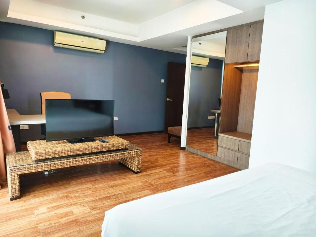 A modern bedroom with a flat-screen TV, a bed, a wicker coffee table, and a wardrobe.