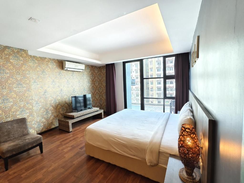 A hotel room with a large bed, a television, a chair, and a window with a city view.