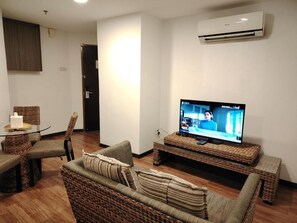 A living room with a television, wicker furniture, and a wall-mounted air conditioner. - Salaam Suites Shah Alam (Shah Alam)
