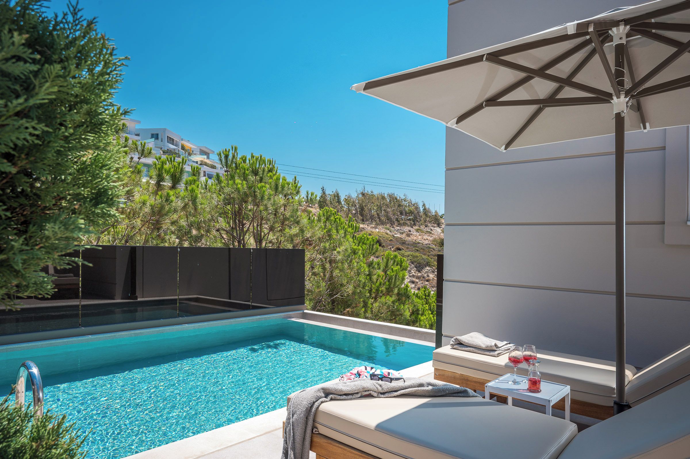 A poolside area with a lounge chair, a table with glasses, and a view of a building in the background.