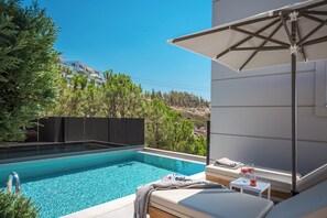Ein Poolbereich mit Liegestuhl, Tisch und Gläsern, im Hintergrund ein Gebäude.
