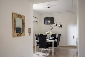 A dining area with a table set for four, black chairs, a decorative mirror, and wall-mounted light fixtures. - Villa Amoudi Private Pool (HERAKLION)