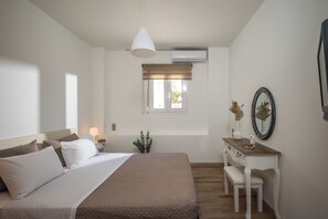 Ein Schlafzimmer mit Bett, Nachttisch, Lampe, Kommode, Spiegel und einem Fenster mit Jalousien.
