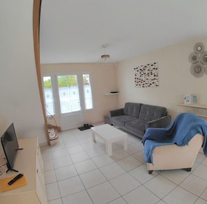 A living room with a grey sofa, a white coffee table, a television, and a door leading outside. - Everything within biking distance & absolute comfort: Bright 3-bedroom, 2-bathroom home with an enclosed courtyard (Le Château-d'Oléron)