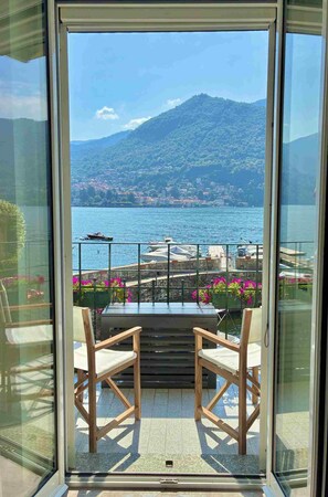 A balcony with a view of a lake and mountains, wooden chairs, and potted flowers. - Vrbo Property (Moltrasio)