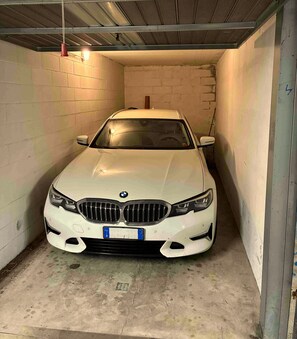 A white car parked in a narrow garage with concrete walls and a metal roof. - Vrbo Property (Moltrasio)