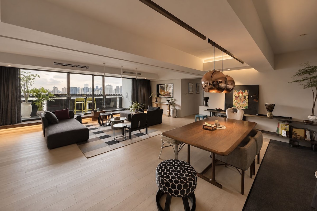 A modern living room with a large dining table, sofas, and a view of the city skyline.