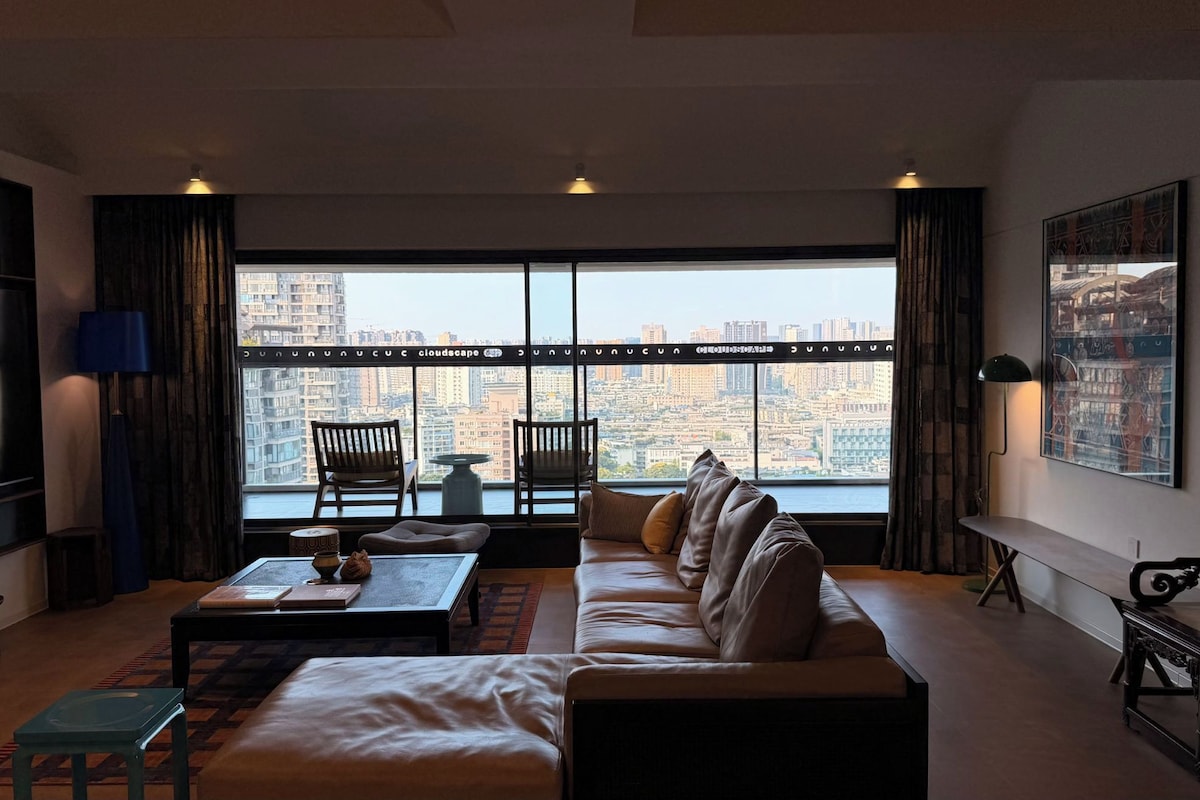 A modern living room with a large window, a sofa, a coffee table, and a television.