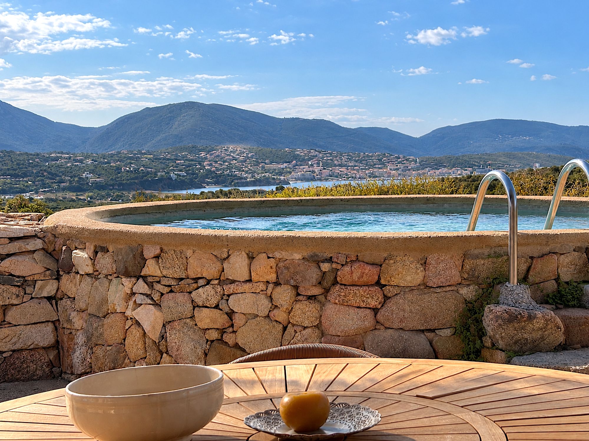 A stone wall with a hot tub and a view of a town and mountains.