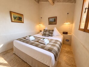 Ein ordentlich bezogenes Bett mit einer karierten Decke und zwei Kissen, ein Nachttisch mit einer Lampe und zwei gerahmte Bilder an der Wand.