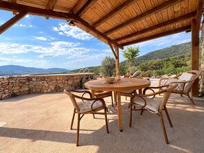An outdoor patio with a round wooden table and wicker chairs, overlooking a mountainous landscape. - Bergerie Firella (Propriano)
