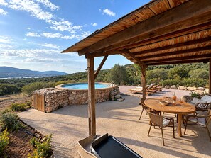 A hot tub surrounded by stone walls, a wooden pergola, and a dining area with outdoor furniture. - Bergerie Firella (Propriano)