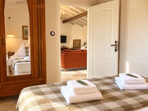 A hotel room with a checkered bedspread, a large mirror, a wooden door, and a view into the adjacent room. - Bergerie Firella (Propriano)